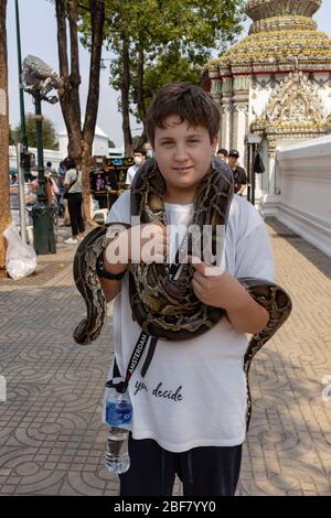 Bangkok, Thailand - February 29th, 2020:A teen aged boy holding a large snake on a Bangkok street. Stock Photo