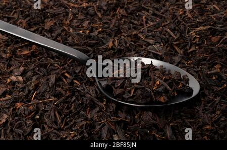 Dry tea leaves in black spoon over dark tea background Stock Photo