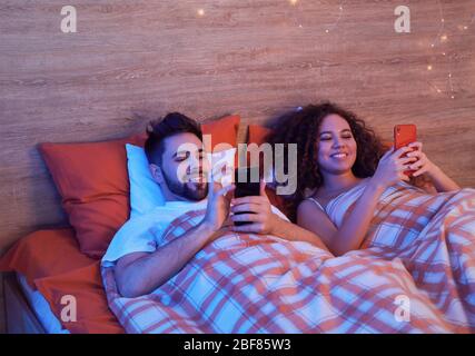 Happy young couple with mobile phones in bedroom Stock Photo