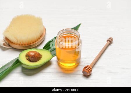 Jar of honey with avocado and massage brush on white wooden background Stock Photo