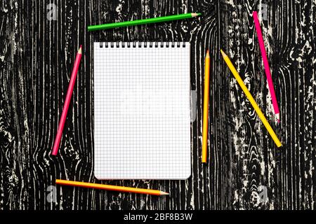 The notebook with squared pages and colorful pencils on a black table with a copy space. Template for mock up and presentation design. Stock Photo