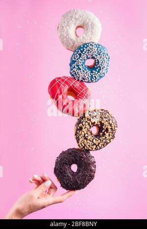 Balancing donuts on the tip of the woman's finger. Multicolored decorated doughnuts in motion flying on pink background. Stock Photo