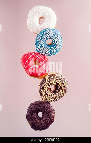 Multicolored decorated doughnuts in motion falling on brown background. Sweet donuts flying in motion. Stock Photo