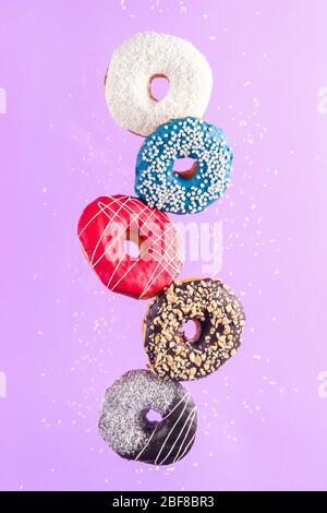 Multicolored decorated doughnuts in motion falling on purple background. Sweet doughnuts flying in motion. Stock Photo