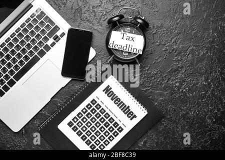 Calendar with alarm clock, laptop, mobile phone and text TAX DEADLINE on dark background Stock Photo