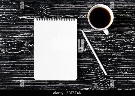 Notebook, pencils and cup of coffee on a black wooden table. Abstract background for design. Art stylized baner or mock up with copy space for a text. Stock Photo