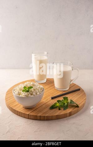 Milk in a cup, kefir in a glass and cottage cheese with herbs in a bowl on a wooden tray on a light background. Copy space Stock Photo