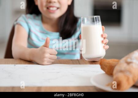 Cute Asian girl with milk showing thumb-up at home Stock Photo