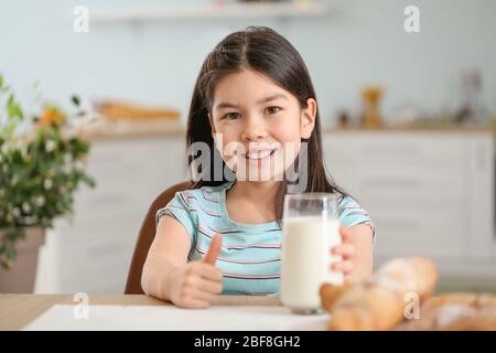 Cute Asian girl with milk showing thumb-up at home Stock Photo