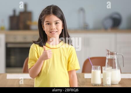 Cute Asian girl with milk showing thumb-up at home Stock Photo