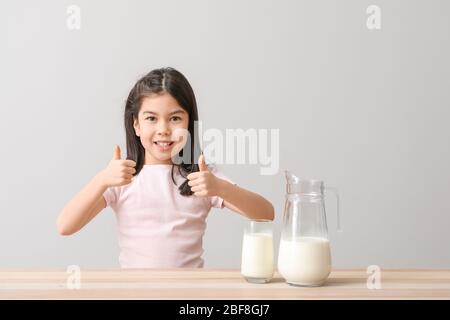 Cute Asian girl with milk showing thumb-up on light background Stock Photo