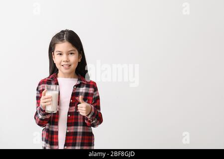 Cute Asian girl with milk showing thumb-up on light background Stock Photo