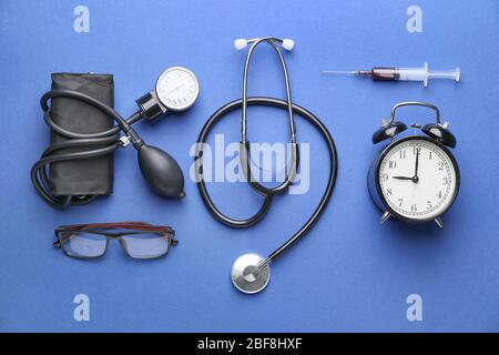 Stethoscope with sphygmomanometer, syringe, alarm clock and eyeglasses on color background Stock Photo