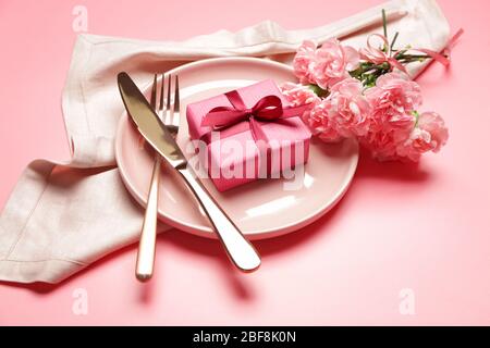 Beautiful table setting with gift and flowers on color background Stock Photo