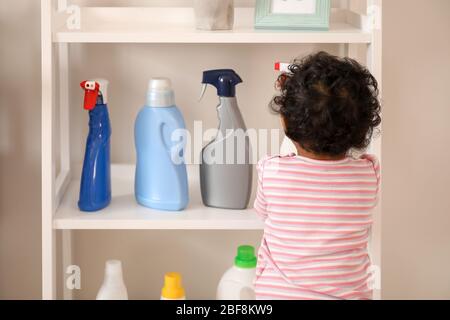 Little African-American baby playing with washing liquids at home. Child in danger Stock Photo