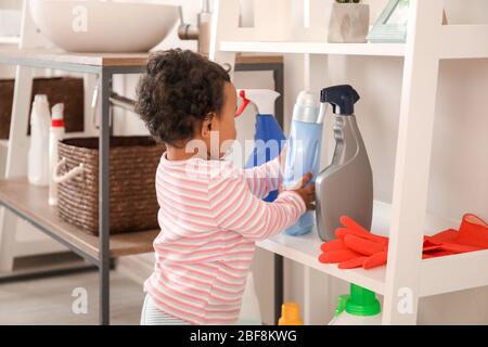 Little African-American baby playing with washing liquids at home. Child in danger Stock Photo