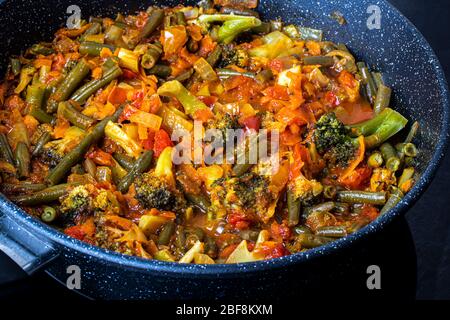 Stewed vegetables in a pan. Cooking process. Vegan food. Broccoli, onions, carrots, green beans and peppers with ketchup. Stock Photo