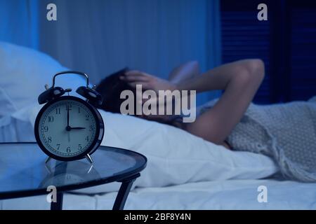 Woman with insomnia lying on bed next to alarm clock at night in apartment Stock Photo