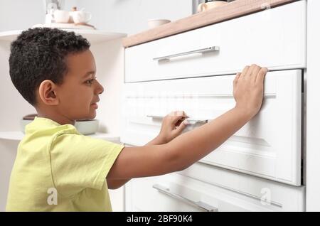 Little African-American boy playing with drawer in kitchen. Child in danger Stock Photo