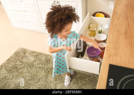 Little African-American girl playing in kitchen. Child in danger Stock Photo