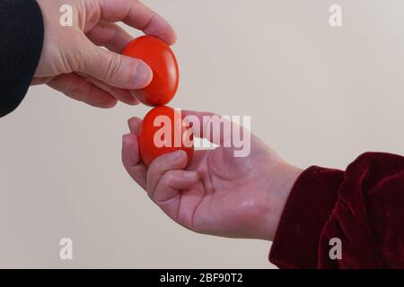 Red hard-boiled eggs tapping Happy Easter game closeup. Two unidentified people hold painted eggs for the knocking egg fight game seasonal tradition. Stock Photo