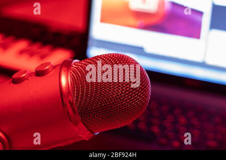 Professional studio condenser microphone on a background of a laptop screen and a music keyboard in red lighting Stock Photo