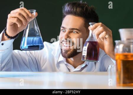 Crazy male alchemist with potions at table Stock Photo