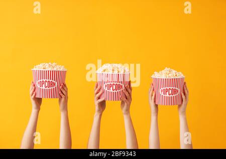Many hands with popcorn in buckets on color background Stock Photo