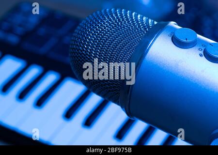 Music tracks production concept. Studio with microphone and synth keyboard on background in blue light Stock Photo