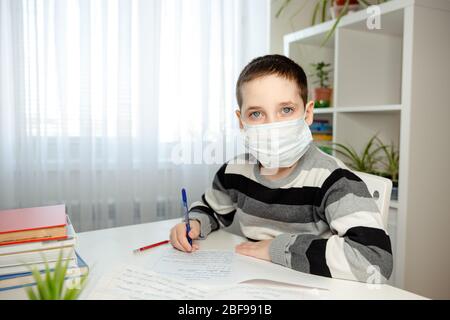 Sickness kid in medical mask studying and doing homework at home Stock Photo
