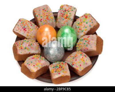 Mini Easter cakes with frosting and colorful sugar sprinkles and three colored eggs in a plate Stock Photo