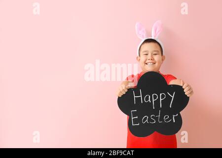 Little Asian boy holding chalkboard with text HAPPY EASTER on color background Stock Photo