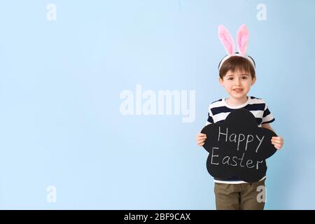 Little boy holding chalkboard with text HAPPY EASTER on color background Stock Photo