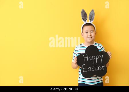 Little Asian boy holding chalkboard with text HAPPY EASTER on color background Stock Photo