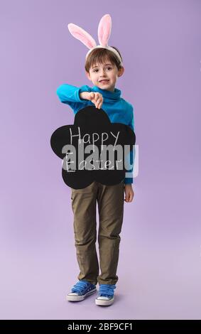 Little boy holding chalkboard with text HAPPY EASTER on color background Stock Photo