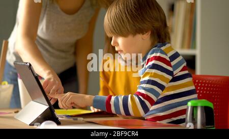 Distance education of children at home during the quarantine period for the coronovirus Covid 19. Mom helps her daughter and son to do homework with a laptop. Stock Photo