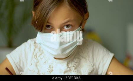 Home training during the quarantine period of the coronavirus Covid19. A girl in a medical protective mask do homework. Close up view. Stock Photo