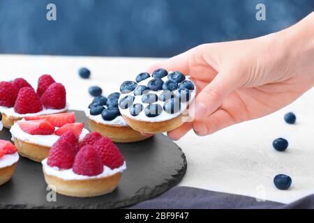 Woman taking tasty cake with berries from table