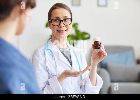 Young smiling doctor with bottle of pills in her hands treating her patient at home Stock Photo