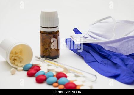 On a white background are surgical gloves, a mask, a thermometer and two jars of pills. Stock Photo