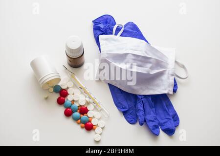 On a white background are surgical gloves, a mask, a thermometer and two jars of pills. Stock Photo