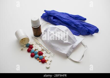 On a white background are surgical gloves, a mask, a thermometer and two jars of pills. Stock Photo