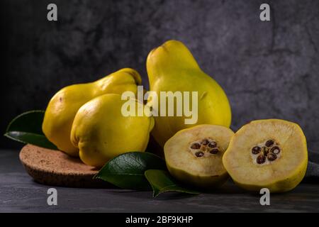 Ripe yellow quinces or queen apple fruits and sliced quince halves with seeds in craft cork plates on black rustic background. Stock Photo