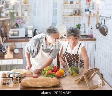 Looking for new recipes. Asian senior elderly couple using digital tablet at kitchen, enjoying cooking together at home in leisure time. Stock Photo