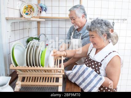Happy asian elder senior couple washing dishes in sink at home in kitchen at home. Stock Photo