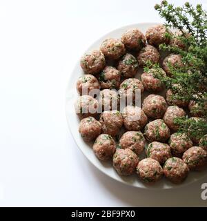 Homemade concept. Fresh raw meat balls on white background. Thyme herbs ornament. Top view. Stock Photo