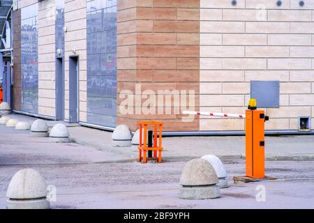 Concrete road barriers and a pneumatic barrier in orange color with a white stripe and red warning stripes, for the entry of cars. Entrance to the cou Stock Photo