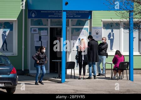 Sofia, Bulgaria. 16 April 2020. Unemployed people wearing protective face masks waiting and filling out forms on impromptu social distancing small tables outside a local job centre of the Department for Social Protection. The unemployment in the country has risen to 7% because of the Pandemic Coronavirus Covid - 19 after years of stable low rates at around 3.5%. Stock Photo