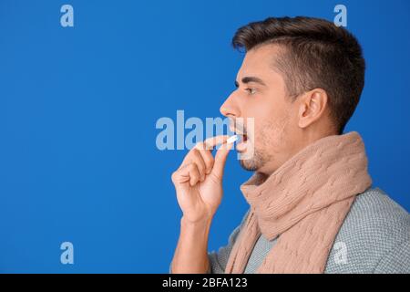 Ill young man taking medicine on color background Stock Photo