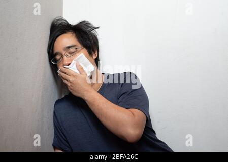 Male Asian young man wearing surgical mask feeling sick headache and coughing leaning on wall isolated on white background.Wuhan coronavirus (COVID-19 Stock Photo